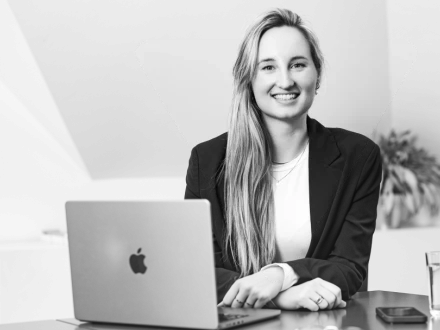 Lächelnde Frau mit langen, glatten Haaren, hellem Oberteil und dunklem Blazer, blickt in die Kamera.